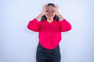 A cheerful woman in a red shirt makes hand binoculars over her eyes while smiling playfully at the camera. photo