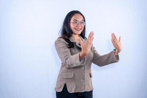 A cheerful woman in a brown jacket and glasses is smiling while making an open hand gesture facing forward. photo