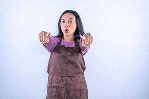 A young Asian woman in a purple shirt and apron points forward with both index fingers. photo
