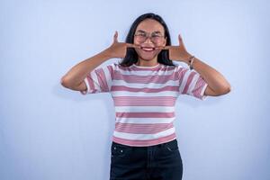 A young woman in a striped shirt smiles widely while using her fingers to stretch her lips into a bigger grin. photo