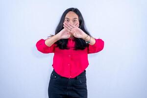 A woman in a red shirt stands with her hands crossed in front of her mouth, signaling silence or refusal to speak. photo
