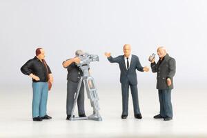 Miniature figure of a male journalist interviewing a businessman, with a cameraman recording photo