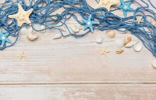 Fishing net, seashells, and starfishes creating a seaside border on wooden planks photo