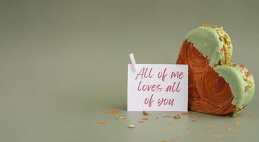 ALL OF ME LOVES ALL OF YOU caption saying in greeting card Delicious fresh croissant topped with Matcha Green Tea flavor Ganache. Creation unique heart shape bakery. Puff pastry holiday love gift present idea Valentine's day. Copy space photo