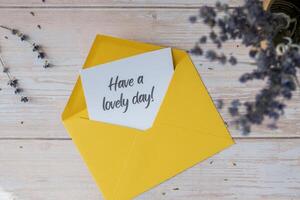 HAVE A LOVELY DAY text on supportive message paper note reminder from yellow envelope. Flat lay composition dry lavender flowers. Concept of inner happiness, slowing-down digital detox personal fulfillment. Top view photo