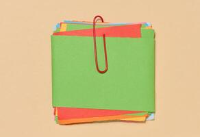 Stack of multi-colored sticky notes secured with a red paper clip, placed on a beige background. photo