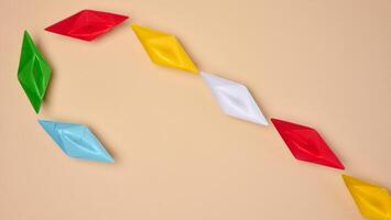 Multi-colored origami paper boats are arranged in a curved line, symbolizing a path or connection photo