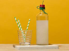 A transparent glass bottle of lemonade stands next to a faceted glass containing three green striped straws. photo