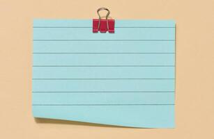 Blue sticky note secured with a red paper clip, centered on a beige background. photo