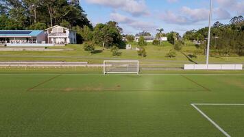 Drone footage captures a soccer field and nearby houses under clear skies, showcasing expansive greenery and serene environment video