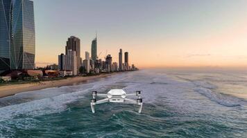 A drone smoothly flies over ocean waves towards a city skyline during a vibrant sunset, capturing serene coastal beauty video