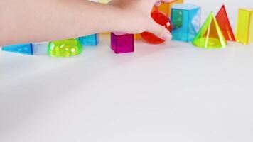 A hand rolls a red sphere among colorful geometric shapes on a white surface, showcasing playful interaction and vibrant colors video