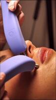 Cosmetic procedure for woman Microcurrents woman's face at beautician. Rejuvenating effect, toned skin, uniform skin color. Close-up, vertical video