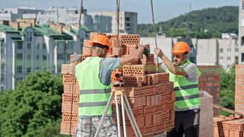 Workers Guiding Brick Load with Crane at Building Site, High-Rise Construction Scene with Safety Gear video