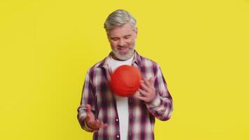 Mature man skillfully bounces basketball on hands, play game, showcasing confident flair, smooth control. Middle-aged guy on yellow background demonstrates athletic finesse, twirling ball on fingertip video