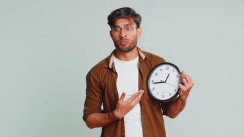 Indian young man with anxiety checking time on clock, running late to work, being in delay, deadline. Arabian guy looking at hour, minutes, worrying to be punctual isolated on studio gray background video