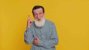 Eureka. Inspired senior old man pointing finger up with open mouth, having good idea, plan, showing inspiration motivation gesture, problem solution. Elderly bearded grandfather on yellow background video