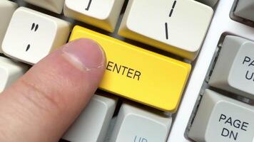 Finger presses the big yellow Enter button on the white keyboard in slow motion, top view video