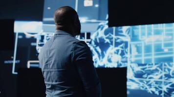 Black IT professional coding for futuristic AI brain blueprints in the background, reflecting AI research through neural networks and deep learning platforms. Algorithmic thinking. Camera B. video