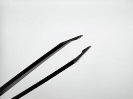 Black metal tweezers with a silver tip on a white background are on the left in the image and in a macro photo