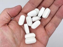 White oblong tablets for illness lie in a man's hand on a white background hand on the left in the image top view photo