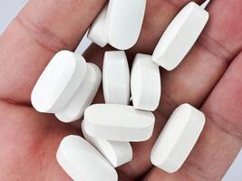 White pills for illness lie in a man's hand on a white background, hand on the left in the image top view macro photo