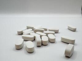 White pills for illness lie on a white background in a scattering and in a pile on the surface, front view photo