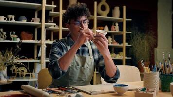 Caucasian man artist designer potter painter guy drawing cup with paintbrush pottery workshop art studio male artisan handmade master class artwork craft painting ornament ceramics sculptor craftsman video