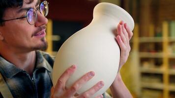 Caucasian man potter craftsman holding handmade clay vase male sculptor smiling satisfied guy male enjoy art work in pottery workshop artisan small business owner craft store sculpting ceramics jug video