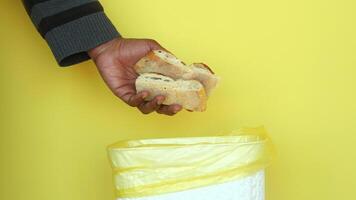 Person discards bread into trash bin in bright setting video