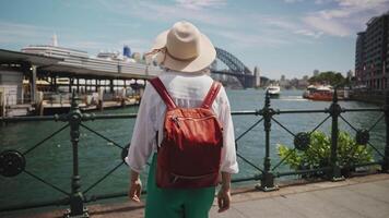 A female tourist stands in Sydney s city center with the iconic Harbour Bridge and sparkling bay as her backdrop. Smiling near the ferry wharf, she embodies summer joy in Australia video