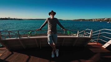 A middle-aged man in a hat and sunglasses stands on the deck of a Sydney city ferry crossing the harbor. Showcases public water transport in action with iconic urban views. video