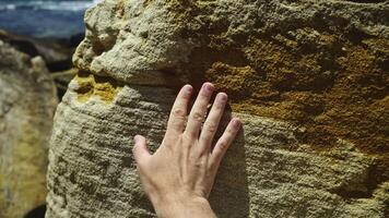 A male hand touches the stunning warm textures of sandstone on a bright sunny day, exploring nature's geological artistry. The rough yet inviting surface video