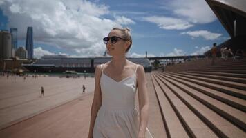 A young, attractive female tourist in a summer dress walks along the steps of the Sydney Opera House, marveling at the breathtaking surroundings video