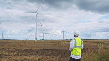 huvud ingenjör undersöker dokumentation för vind bruka och dess operativ metrik, stående i en nytt bearbetad jordbruks fält. video