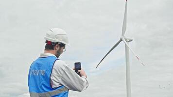 Young male blogger visits a wind farm and takes pictures of it with his phone. He creates interesting environmental content to share on his social media platforms. video