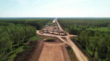 Aerial view of an unfinished overpass bridge under construction as part of a highway development project through a forested area, surrounded by trees and rural landscape. video