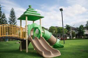 Colorful playground structure featuring green slides and climbing area, set in a lush green park with trees and blue sky in the background photo