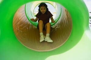 Child slides down colorful playground tube, happy expression, sunny day, outdoor fun, childhood adventure, playful moment captured in vibrant setting photo