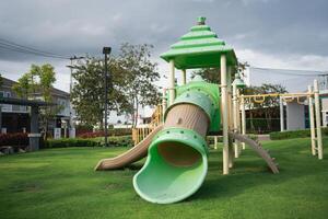 Vibrant Play Area with Green Slide and Tower in Outdoor Park Surrounded by Grass and Trees Under a Cloudy Sky photo