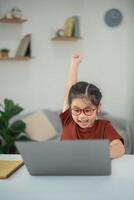 Excited Child Celebrating Success While Using Laptop in Cozy Indoor Environment with Plants and Shelves in Background photo