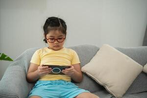 Focused Young Girl Engaged in Interactive Game on Smartphone While Sitting Comfortably on Soft Couch Surrounded by Bright Indoor Space photo