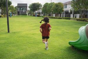 Joyful Child Running in Park with Vibrant Green Grass and Play Equipment, Bright Sunny Day, Outdoor Activity, Happiness and Freedom Experience photo