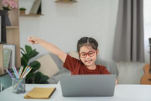 Happy child celebrating success while studying at home using laptop, showcasing joy and enthusiasm in a bright and welcoming environment photo