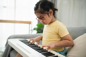 Young girl in yellow shirt playing keyboard indoors with focus and concentration, exploring musical talent and creativity while sitting on a cozy sofa photo