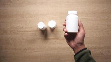 Holding a white supplement bottle with two others on a table video