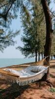 Hammock with fringes sways gently from a tree on a sunny beach, with the vibrant blue sea and sky in the background, perfect for relaxation and leisure photo
