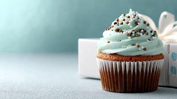 A cupcake with white frosting and sprinkles sits next to a gift box photo