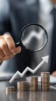 Businessman holding magnifying glass over stacks of coins photo