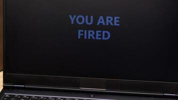 Close-up of laptop screen displaying bold 'YOU ARE FIRED' message. video